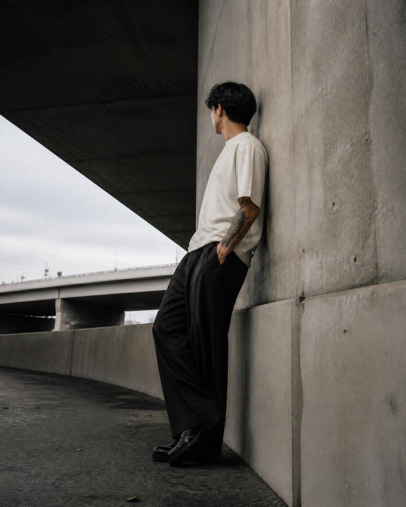 Placeholder campaign image: model in a cream heavyweight tee and black wide-leg trousers against concrete